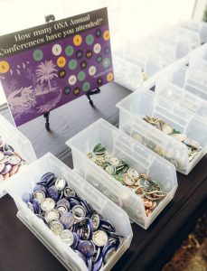 A sign on a tabletop easel asks, How many ONA Annual Conferences have you attended? In front of it are plastic bins holding buttons, each with a number representing the number of conferences someone has attended